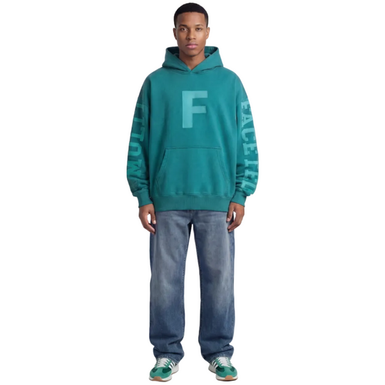 Person wearing a teal hoodie with a logo on a white background