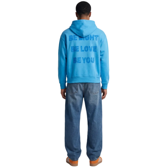 Person wearing a Turquoise blue hoodie with motivational text on the back, standing against a white background