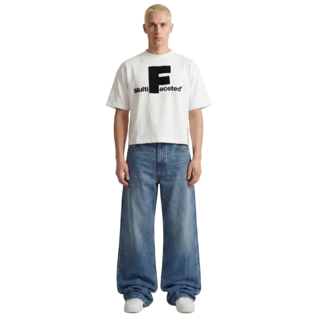 Person wearing a white t-shirt with a logo and text, paired with blue jeans on a plain background