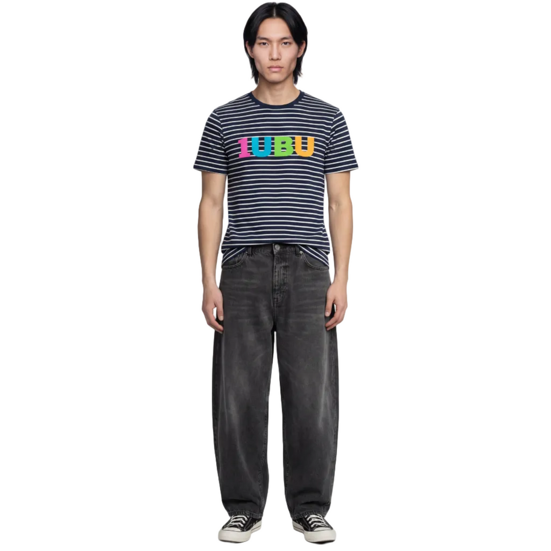 Person wearing a striped shirt with colorful text and dark jeans on a white background