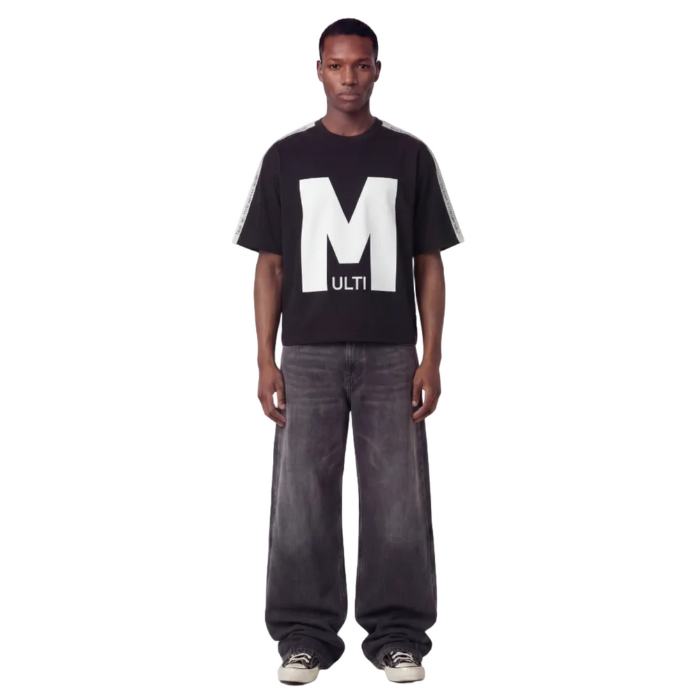 Person wearing a black t-shirt with a large white letter 'M' and gray jeans on a white background