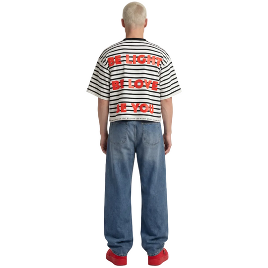 Person wearing a striped shirt with text and blue jeans on a white background